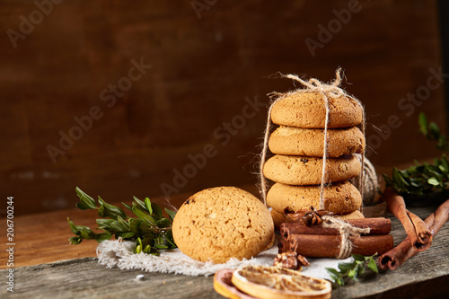 Christmas composition with pile of cookies, cinnamon and dried oranges on light wooden background, close-up.