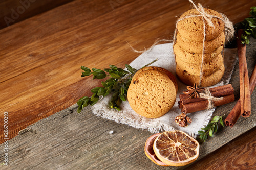 Christmas composition with pile of cookies, cinnamon and dried oranges on light wooden background, close-up.
