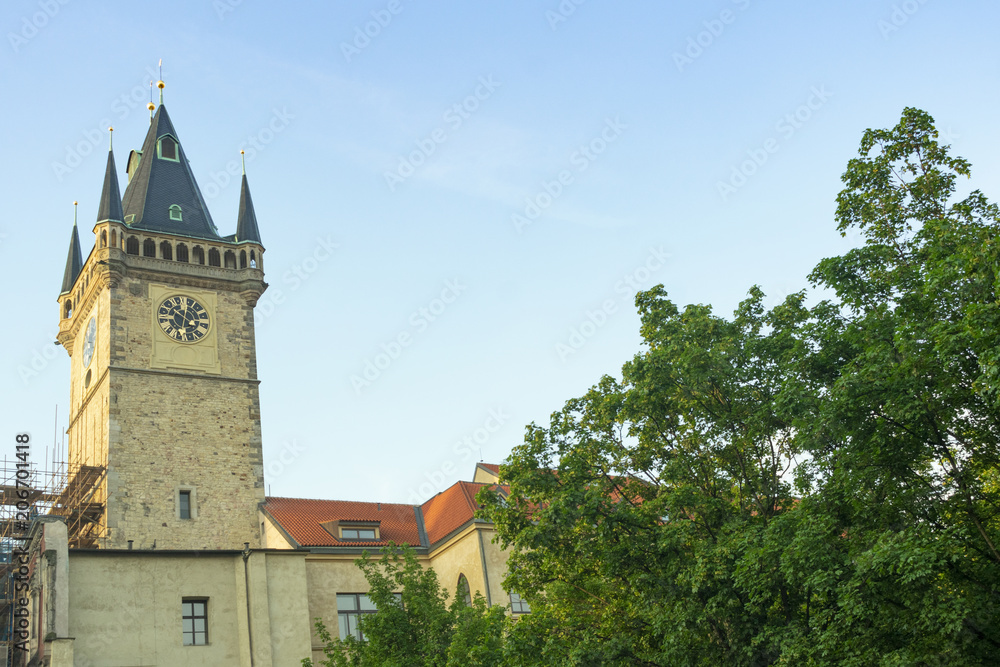 Prague, Czech Republic, an old stone tower with a clock in the center of the city against the blue sky and green trees