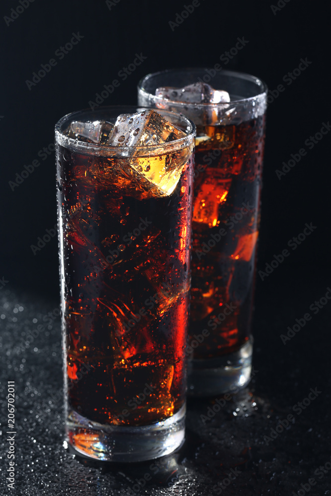 Glasses of cola with ice cubes on black stone
