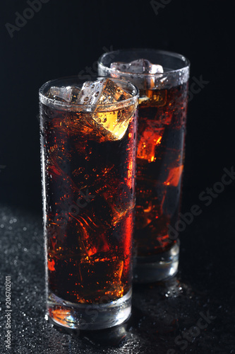 Glasses of cola with ice cubes on black stone