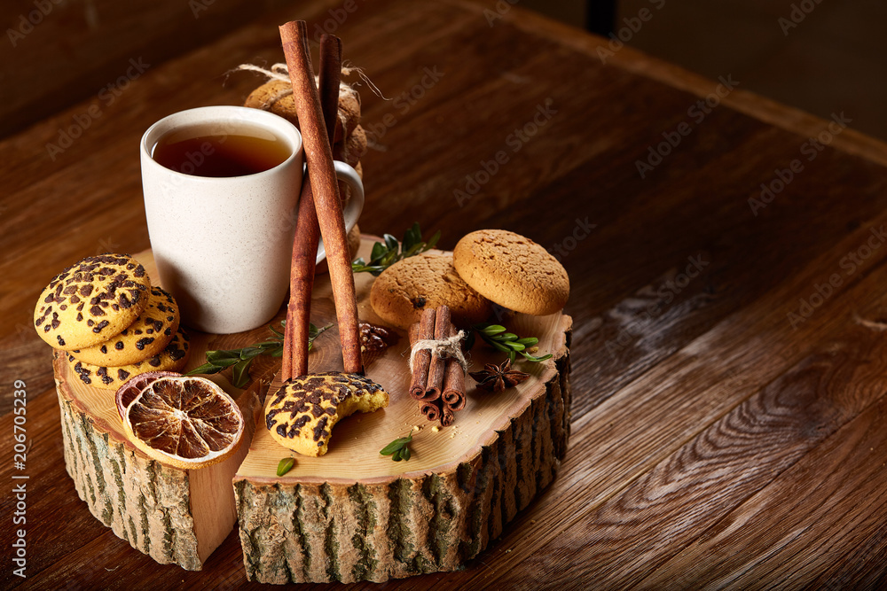 Christmas concept with a cup of hot tea, cookies and decorations on a log over wooden background, selective focus