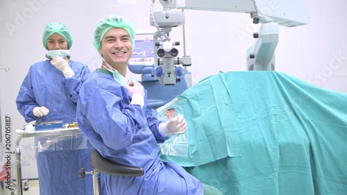 Surgeon operating lasik machine portrait. Young white male surgeon operating lasik machine on a senior patient with chinese female nurse. Smile and look at camera. Sliding dolly shot.