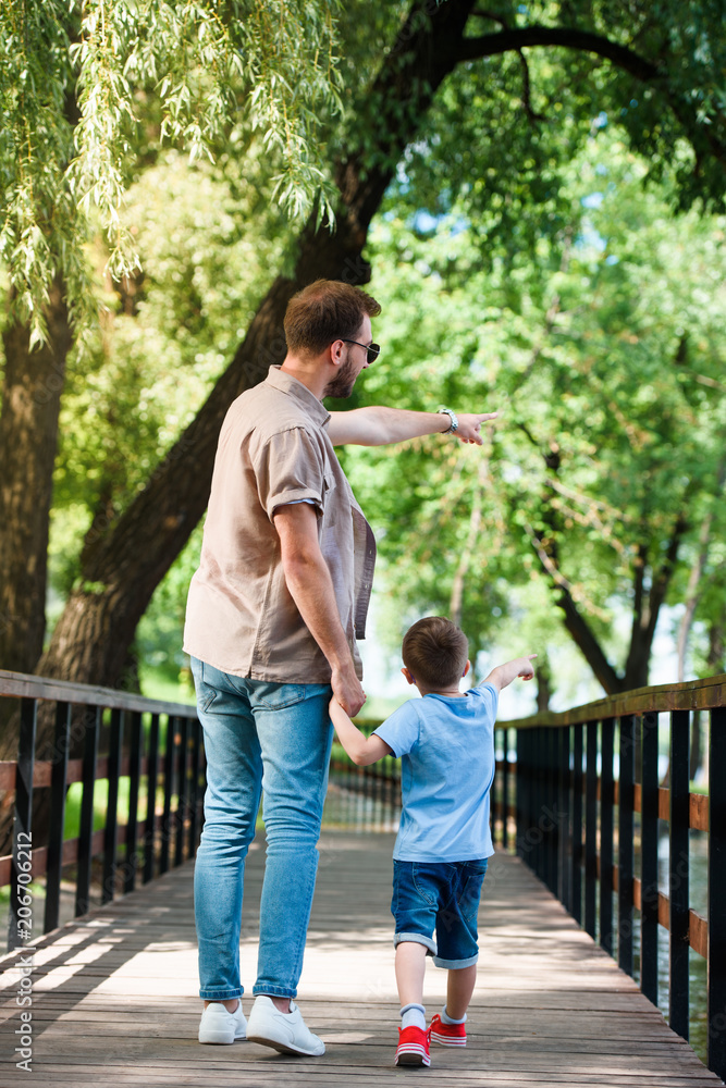 back view of father and son pointing on something on bridge at park back view of father and son pointing on something on bridge at park