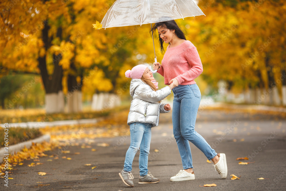Fototapeta premium Young pretty mother with her little daughter having fun in the fall background. Happy family in autumn
