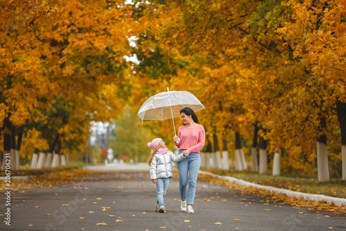 Young pretty mother with her little daughter having fun in the fall background. Happy family in autumn