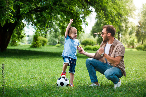 happy father and son showing yes sign after playing football at park
