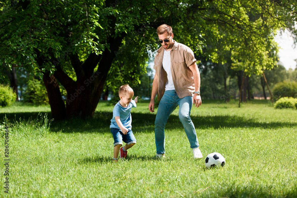 father and son playing football on grass at park father and son playing football on grass at park