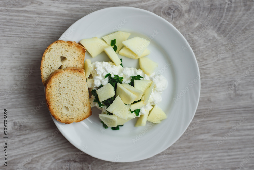 Natural delicious breakfast. Fried slices of baguette with curd, apple slices and parsley on a white plate, wooden background