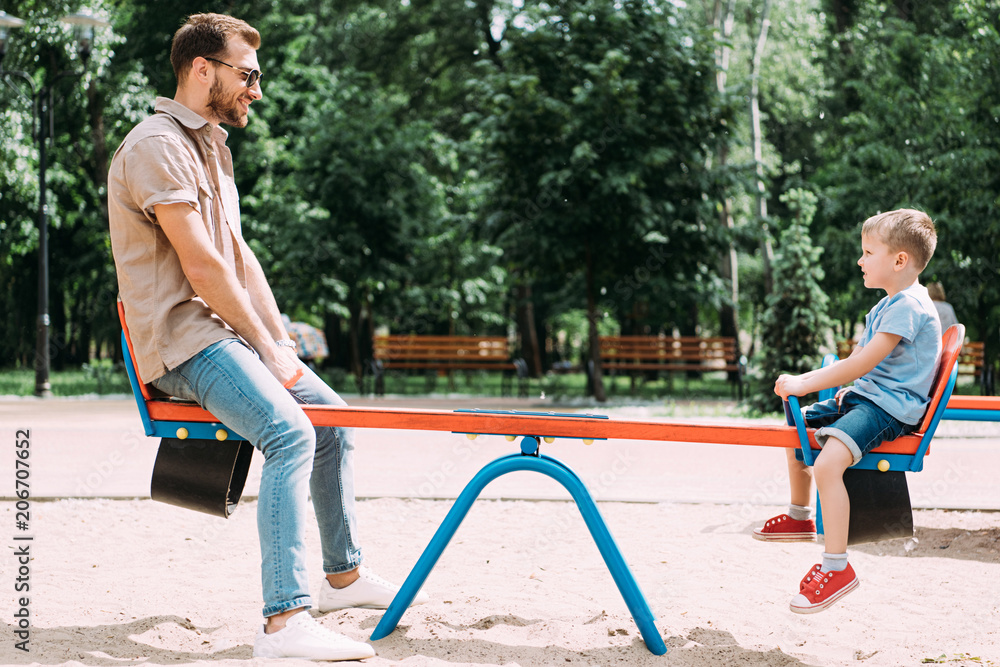 side view of father and son having fun on swing at playground in park side view of father and son having fun on swing at playground in park