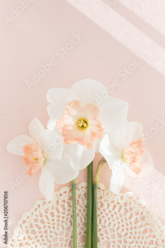 Fototapeta Naklejka Na Ścianę i Meble -  Delicate bouquet of three Orchid daffodils on pink background with crochet napkin, minimalistic creative pastel concept, square, hard light