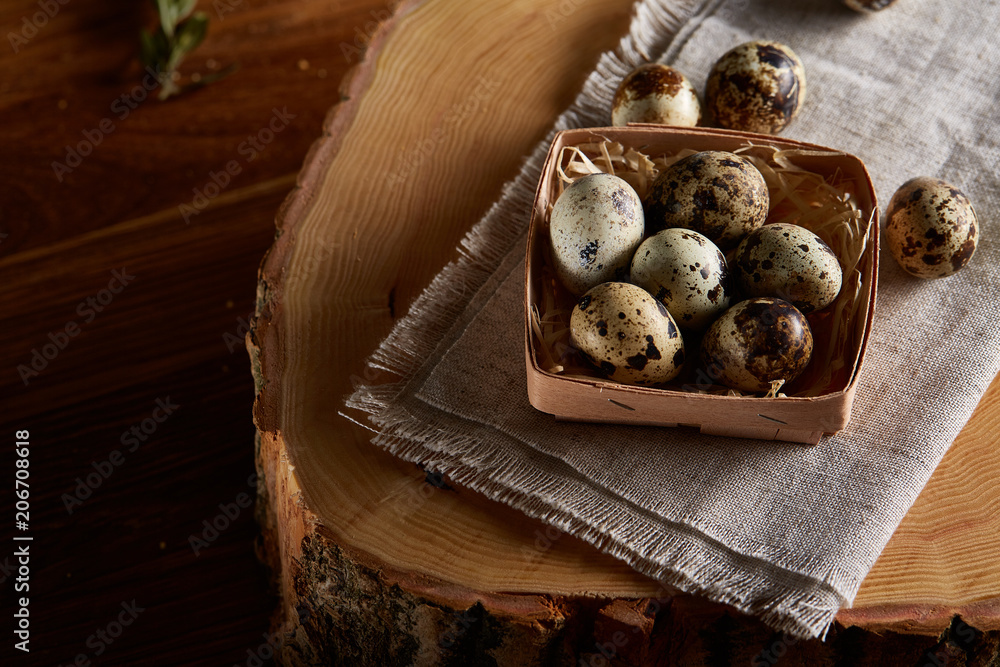 Composition of eggs quail box, eggs on a homespun napkin on a log over wooden background, top view Composition of eggs quail box, eggs on a homespun napkin on a log over wooden background, top view
