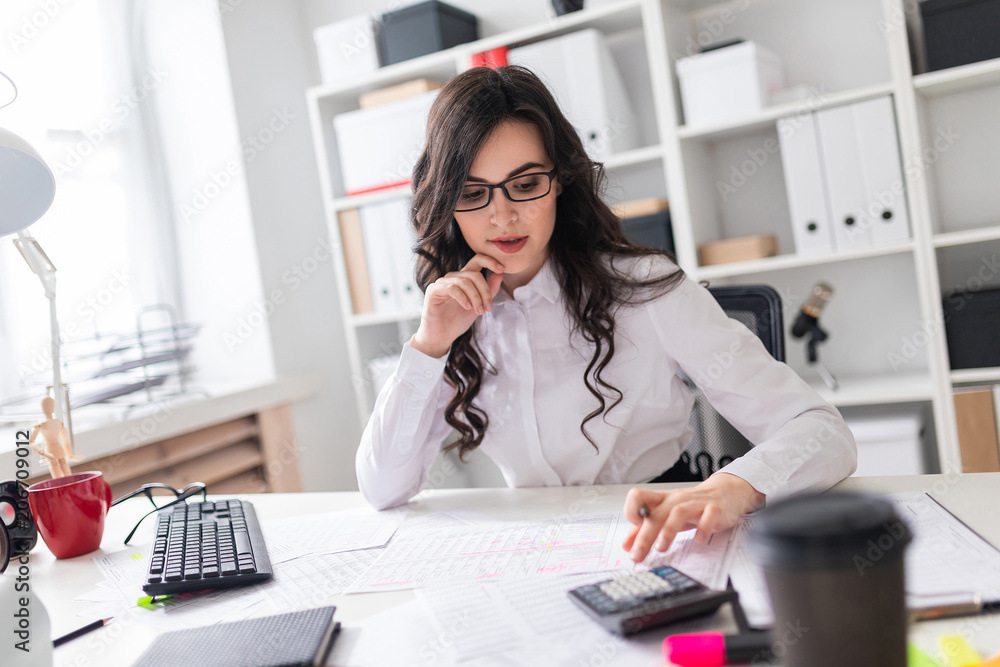 A young girl is sitting at the office desk and is blessing on the calculator. A young girl is sitting at the office desk and is blessing on the calculator.