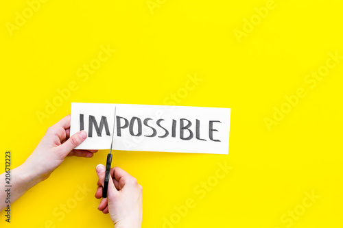 All is possible concept. Hands cutting the part im of written word impossible by sciccors. Yellow background top view copy space