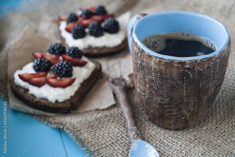 Sandwiches with sweet cheese and berries, a cup of coffee in blue wooden background Sandwiches with sweet cheese and berries, a cup of coffee in blue wooden background