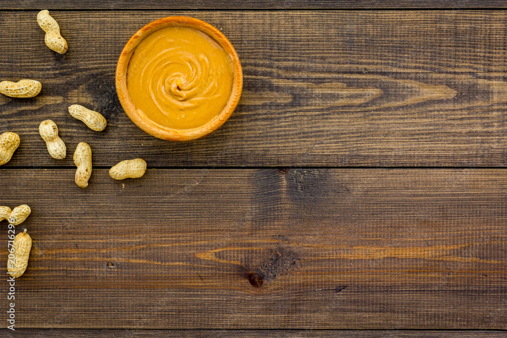 Product for hearty breakfast. High-calorie product. Peanut butter in bowl near nuts in shell on dark wooden background top view space for text Product for hearty breakfast. High-calorie product. Peanut butter in bowl near nuts in shell on dark wooden background top view space for text