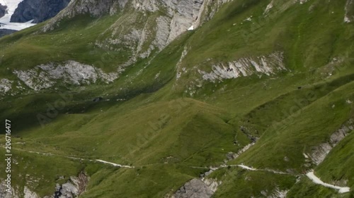 Alpine mountain side time lapse: dozens of hikers and bikers climbing and descending a mountain path while the shadows of clouds pass by. photo