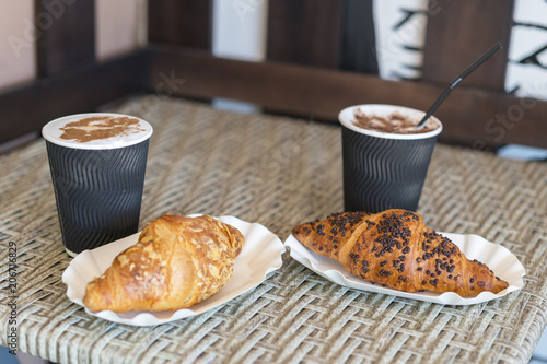 Cappuccino with croissant. Two cups of coffee with milk foam stands on a table in cafeteria. Two cups of coffee and two croissants on the street in Croissant Cafe. Inscripton on cup - Croissant Cafe. photo