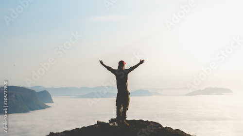Young man stand on top of mountain top with hands raised in the air. Success and risk concept.