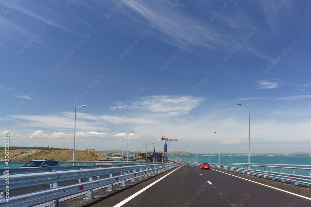 Cars go on the Crimean bridge across the Kerch Strait. On the left is the construction of the railway bridge
