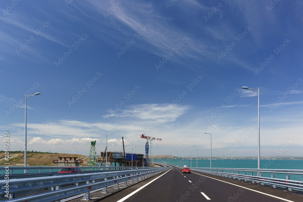 Red Car rides on the Crimean bridge across the Kerch Strait. On the left is the construction of the railway bridge