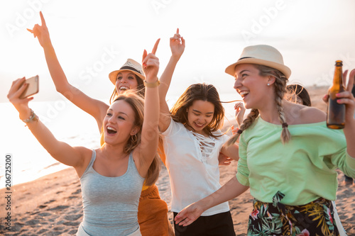 Happy multiracial young women making a selfie at the beach while they are in a summer party. Friends and holiday concept