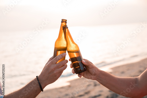 Cheers! Close up of hands toasting with bottles of beer in the beach. Celebration concept photo