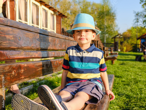 Smiling child sitting on a park bench with green meadow on background