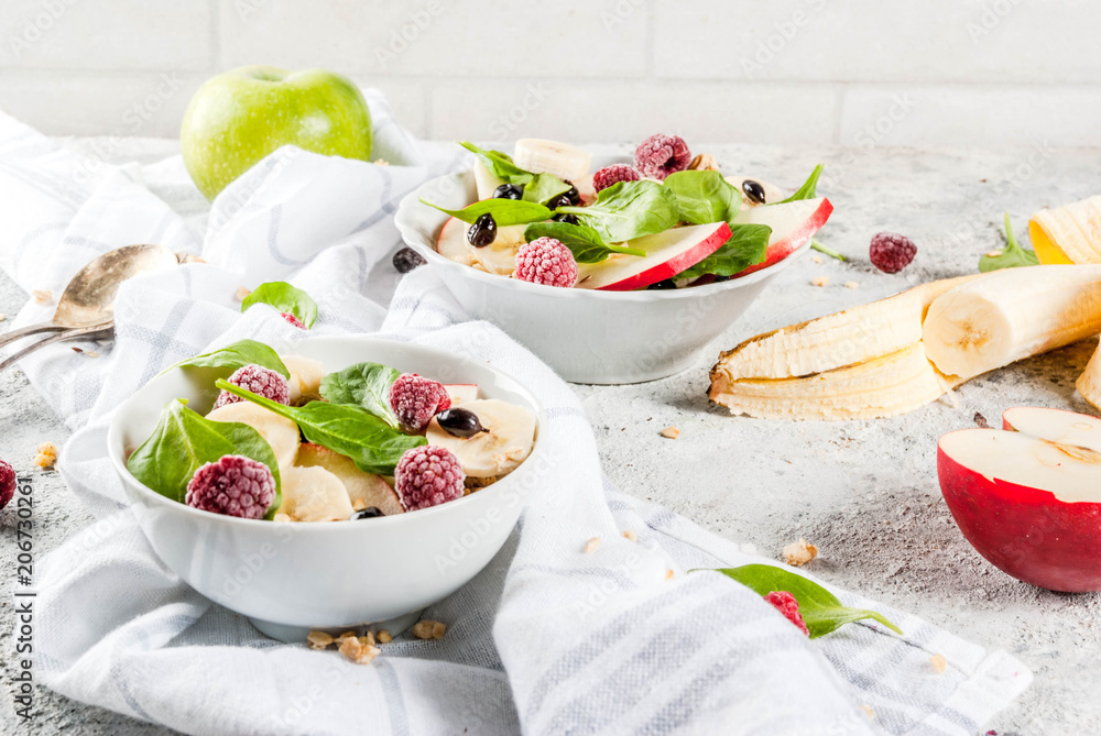 Healthy summer breakfast, fruit and berry salad with spinach, granola, apple and banana, white marble background  copy space