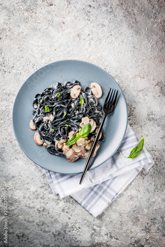 Modern italian dinner, Mediterranean food, black cuttlefish ink spaghetti pasta with champignon mushrooms, olive oil and basil,  on grey stone table top view copy space