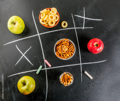 Tic tac toe healthy and unhealthy snack concept with crackers, chips and apples on black chalkboard