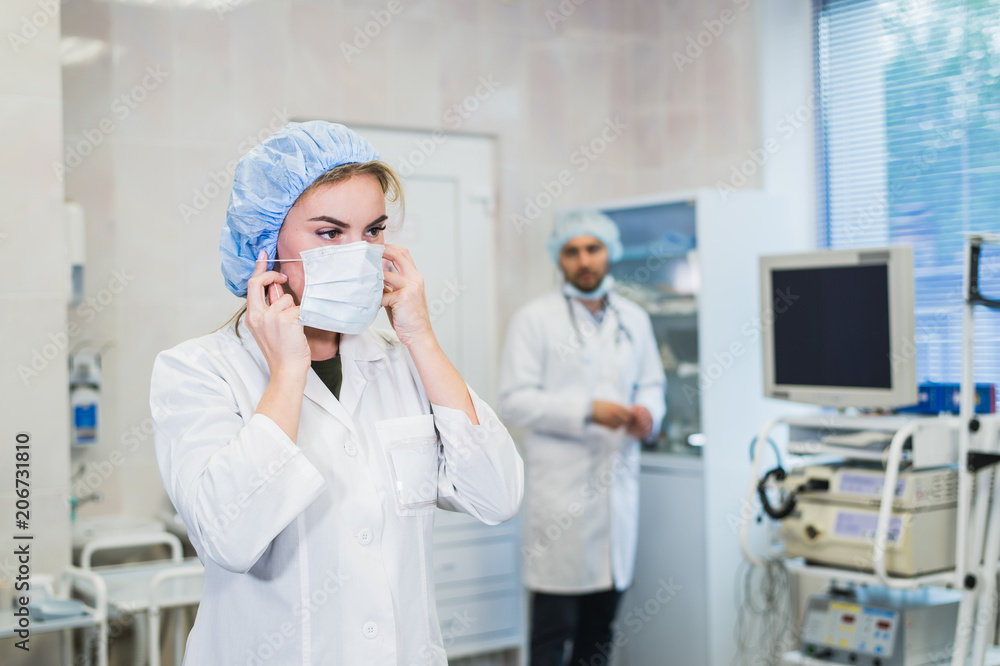 Team of doctors is being prepared for the operation. The nurse assistant wearing mask. Doctor preparing equipment on the background. Concept of health, work in the hospital. Team of doctors is being prepared for the operation. The nurse assistant wearing mask. Doctor preparing equipment on the background. Concept of health, work in the hospital.