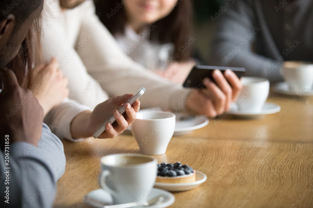 Diverse people using smartphones sitting at cafe table together, friends holding gadgets enjoying new apps or checking social networks at meeting connected online to public place wifi, close up view Diverse people using smartphones sitting at cafe table together, friends holding gadgets enjoying new apps or checking social networks at meeting connected online to public place wifi, close up view
