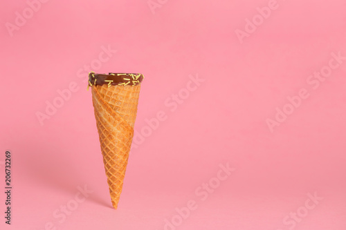 funny creative concept of close up empty wafer cone with chocolate glaze and colorful sprinkles over pastel pink background
