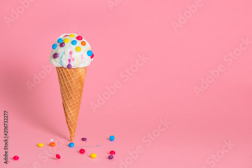 summer funny creative concept of wafer cone with melting ice cream covered and strewed colorful chocolate confetti on pink background