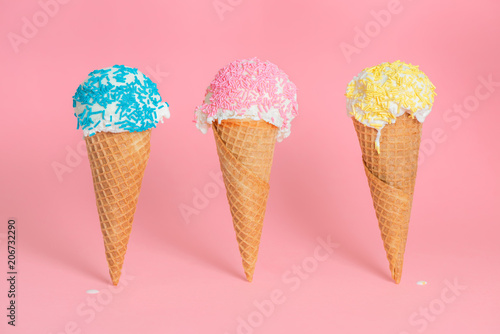 funny creative concept of close up three wafer cups with melting ice cream and colorful sprinkles over pastel pink background