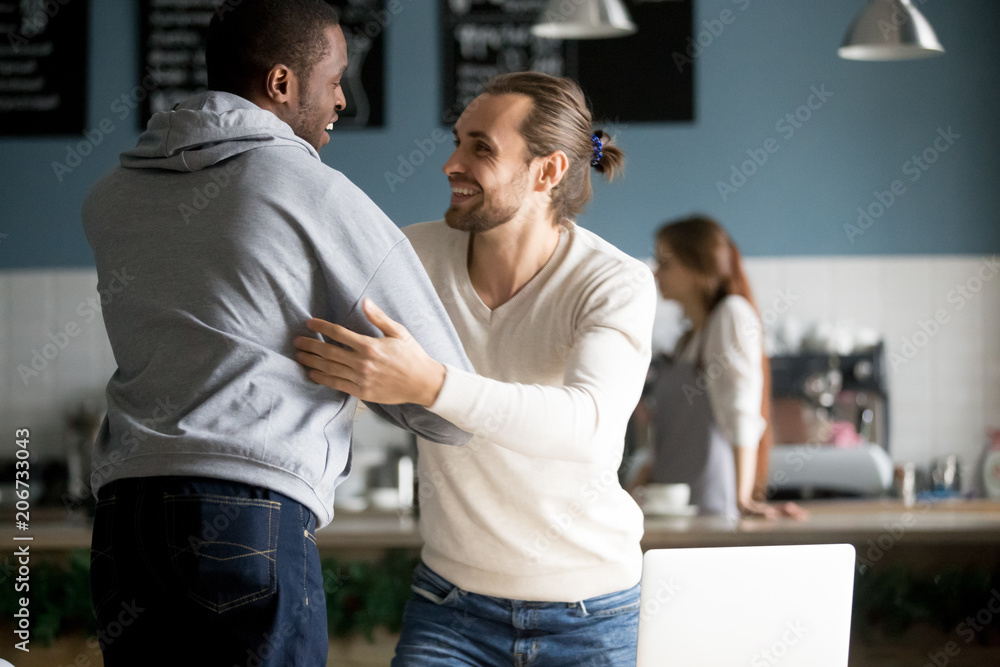 Smiling diverse male buddies embracing greeting in cafe, happy millennial men best friends reaching to hug saying hello welcoming at meeting in cafeteria, good friendly relations and reunion concept Smiling diverse male buddies embracing greeting in cafe, happy millennial men best friends reaching to hug saying hello welcoming at meeting in cafeteria, good friendly relations and reunion concept
