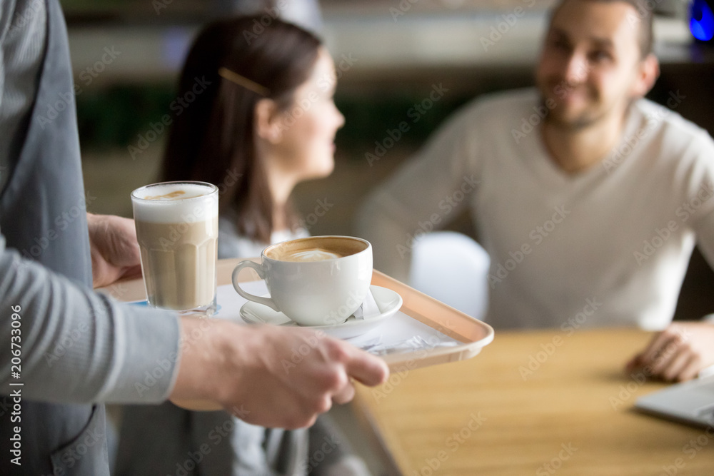 Waitress holding tray with cappuccino and latte, female hands serving hot aromatic brewed coffee drinks to couple visitors waiting at cafe table, coffee house shop service concept, close up view Waitress holding tray with cappuccino and latte, female hands serving hot aromatic brewed coffee drinks to couple visitors waiting at cafe table, coffee house shop service concept, close up view
