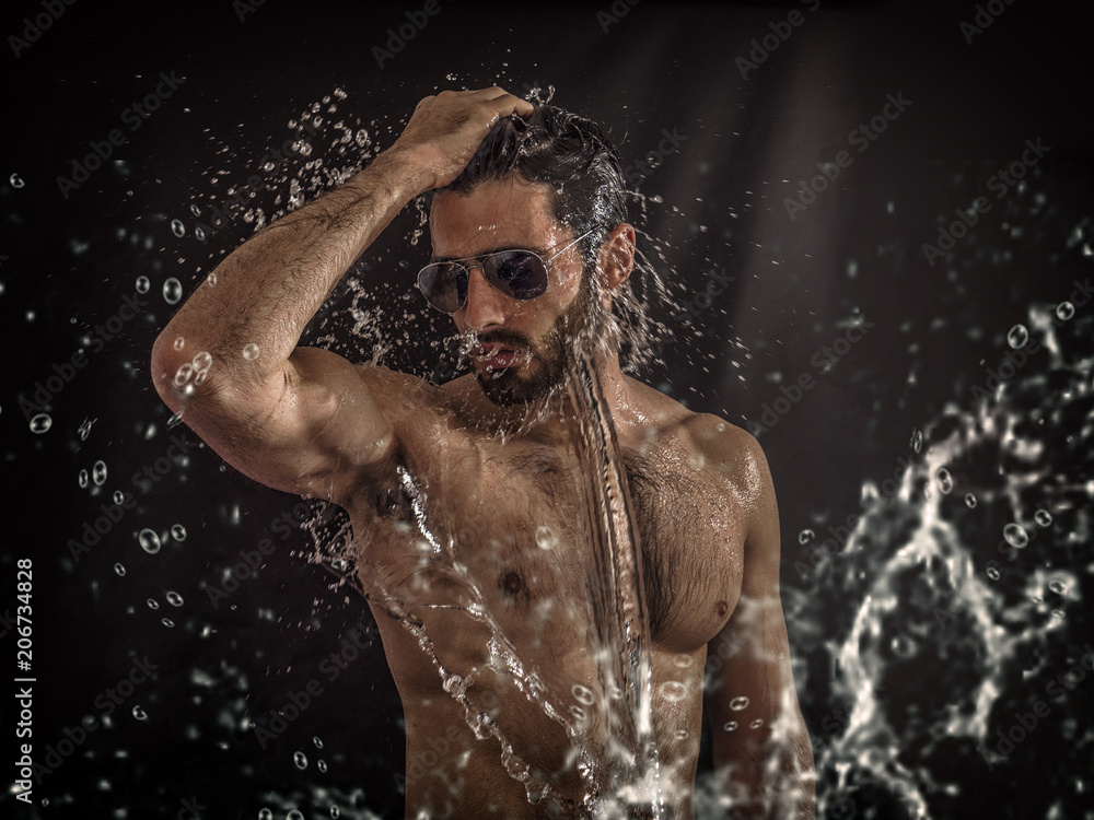 Shirtless handsome young man with water splashes on his face and chest in studio shot - obrazy, fototapety, plakaty 