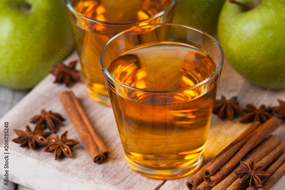 Apple juice in glasses, spices and apples on wooden cutting table Apple juice in glasses, spices and apples on wooden cutting table