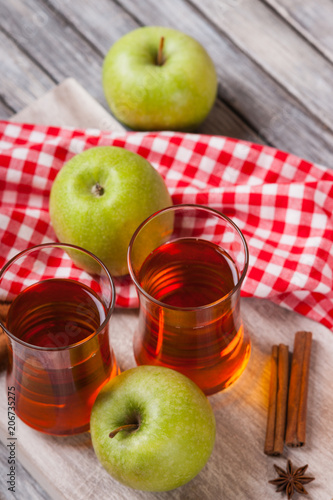 Apple juice in glasses, spices and apples on wooden cutting table 