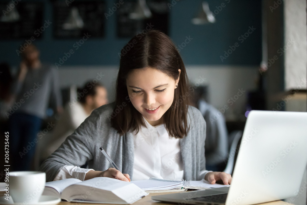 Smiling millennial girl making notes in exercise book sitting at coffee shop table, happy positive student writing down summary or essay studying in cafe, easy interesting self education concept Smiling millennial girl making notes in exercise book sitting at coffee shop table, happy positive student writing down summary or essay studying in cafe, easy interesting self education concept