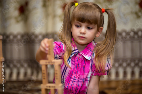 Little girl play with wooden blocks. Kid inspecting wooden block buildings, childhood activities. Tower stack from wooden blocks toy and girl's hand take one block