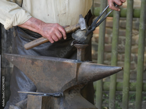 steel anvil, on top of which lies a hot workpiece, the hand of the blacksmith processes a workpiece with the aid of a hammer and pliers , the hammer strikes straight, it has some motion blur ,