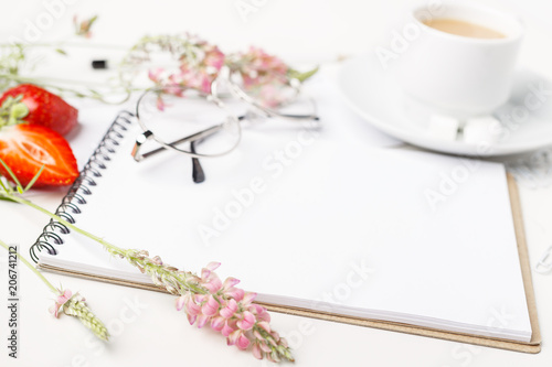 Flowers, notepad, glasses and tea with milk in white cup on a white table. Flatlay. Top view. For design.