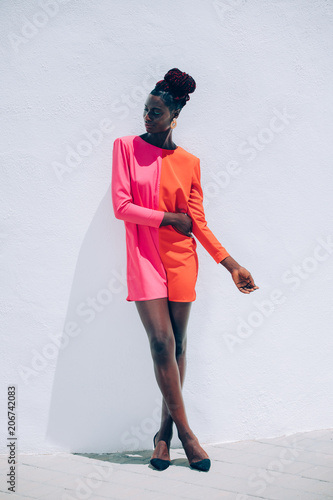 Exotic portrait of a beautiful and attractive black model woman wearing a red and pink dress with a fashion makeup posing on white background. Exotic fashion concept