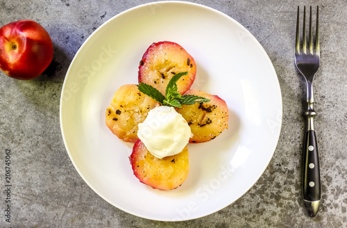 Baked peaches with ice cream on a plate on a gray metal background