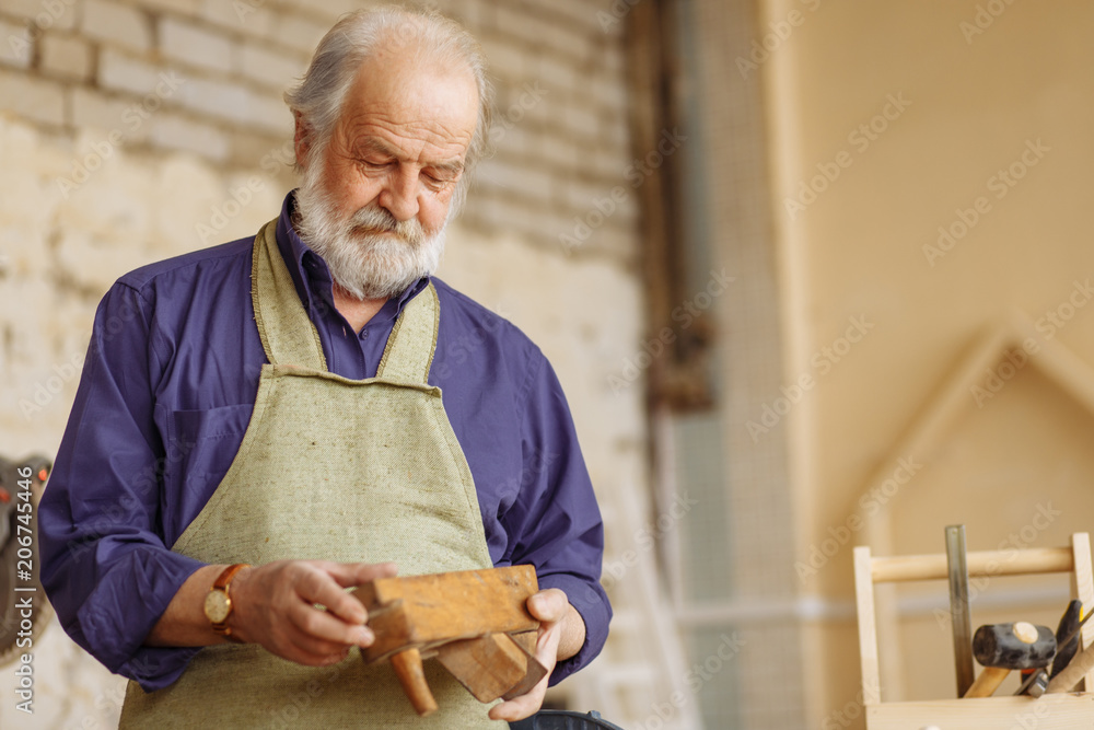 old man in casual clothes and apron is looking at the wooden plane and  checking it in the garage Stock Photo | Adobe Stock