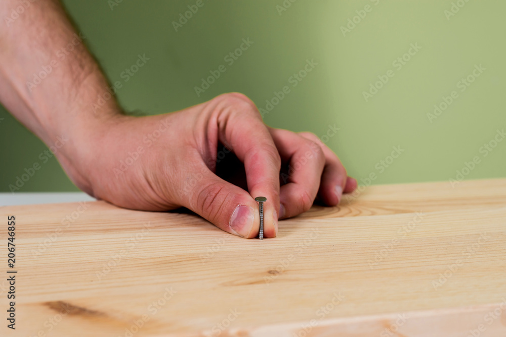 Hammering a nail into wooden plate. Concept of renovation, housework. The man is holding a blue hammer in his hand, holding a nail in the other hand. Handyman, DIY. Hammering a nail into wooden plate. Concept of renovation, housework. The man is holding a blue hammer in his hand, holding a nail in the other hand. Handyman, DIY.