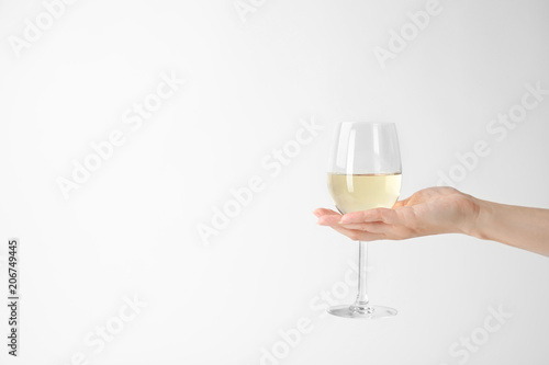 Woman holding glass of expensive white wine on light background